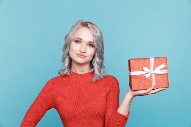 Cute female holding red gift box on the blue background