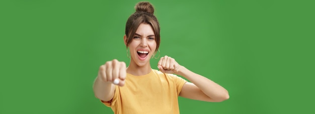 黄色いTシャツを着た可愛い女性の反乱者歯の隙間で拳をカメラに向け戦いを示しているかのように引いています