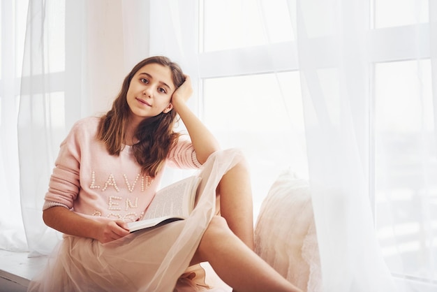 Cute female teen sits indoors in the living room with book at holidays time.