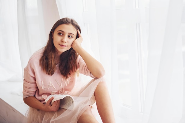 Cute female teen sits indoors in the living room with book at holidays time.