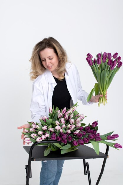 Cute florist girl in a shirt collects a bouquet of purple and white tulips for a birthday present