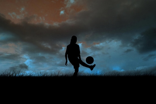 Cute football player kicking ball against blue sky over grass