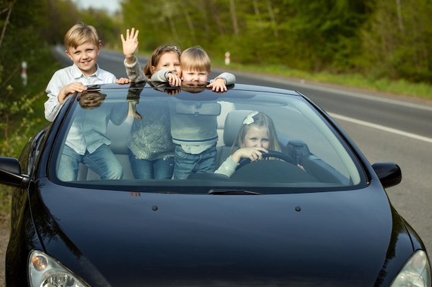 Photo cute four baby children friends of girls and boys people with at wheel pretends driving car as drivers on road outdoor