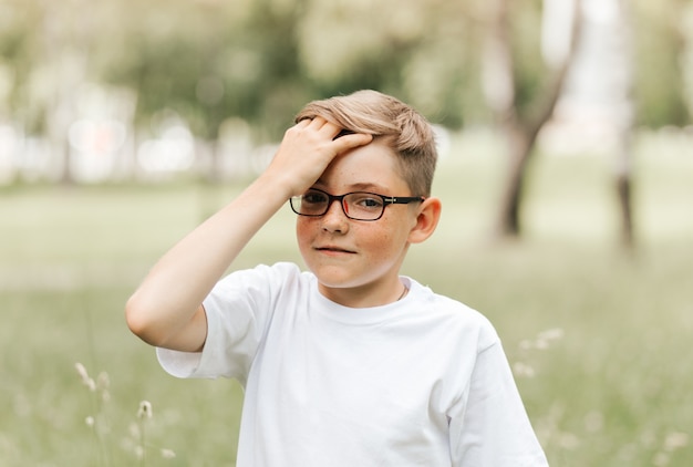 Симпатичный веснушчатый мальчик в очках держится за голову.