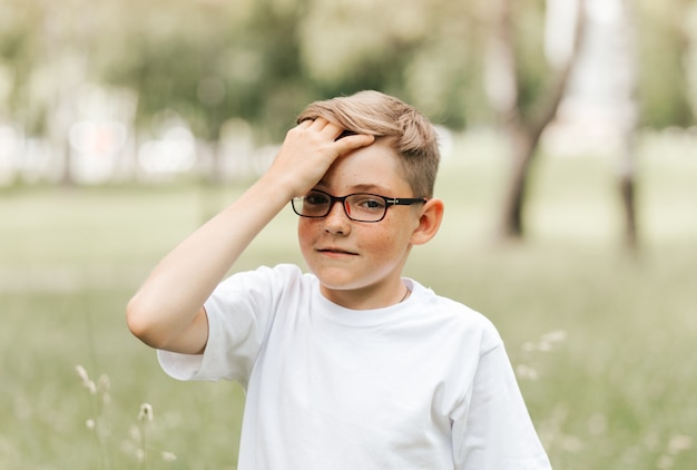 眼鏡をかけたかわいいそばかすの男の子が頭を抱えています。