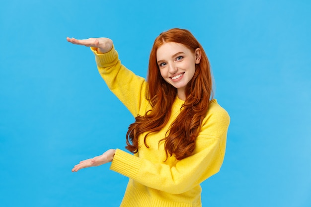 Cute friendly-looking caucasian redhead woman shaping large object with hands