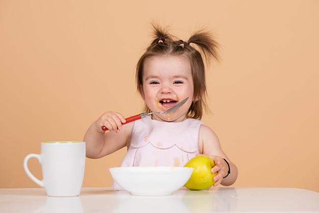 이유식을 먹는 귀엽고 재미있는 아기 숟가락을 들고 웃긴 웃는 아기 소녀가 스스로 먹는다