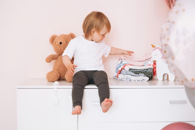 Foto bambino felice della neonata divertente sveglia in vestiti domestici che si siedono sul comò a casa