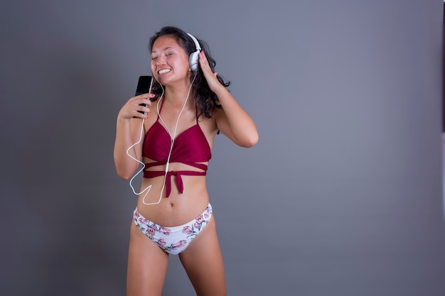 Симпатичный и забавный китаец в бикини слушает музыку со смартфона и наушников