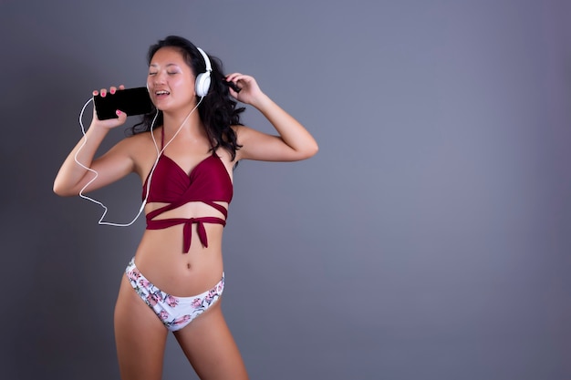 Cute and funny chinese in bikini listening to music from smartphone and headphones