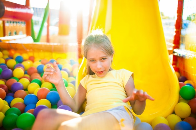 Photo a cute funny girl sits in a playground with soft and bright equipment and throws colorful balls towards the camera