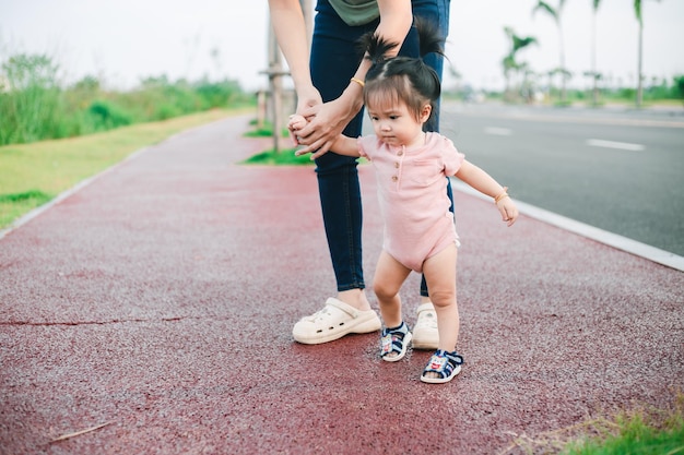 공원에서 첫 발걸음을 는 귀여운 재미있는 행복한 아기 엄마가 는 것을 배우면서 그녀의 손을 들고 지원하는 고품질의 이미지 는 개념을 배우십시오 엄마와 어린 소녀
