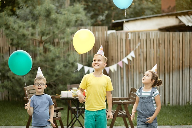 Cute funny kids celebrating birthday with family or friends in a backyard Birthday party Kid wearing party hat and launch balloons into the sky