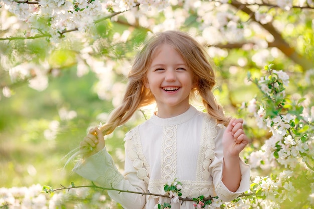 a cute funny little girl in a dress in spring near a flowering tree is laughing gentle photography