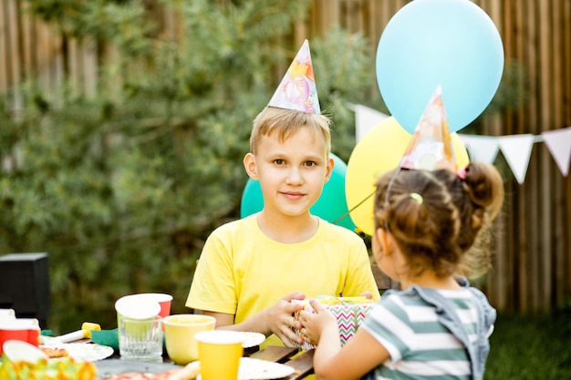 Ragazzo carino e divertente di nove anni che festeggia il suo compleanno con la famiglia o gli amici con una torta fatta in casa in una festa di compleanno per bambini nel cortile