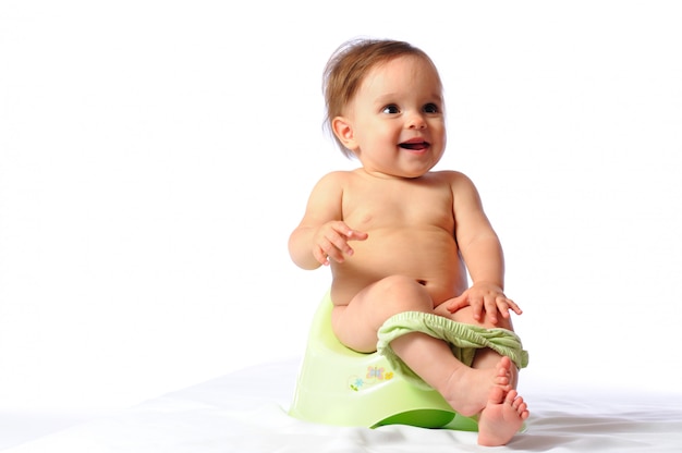 Cute funny one year baby sitting on green potty.