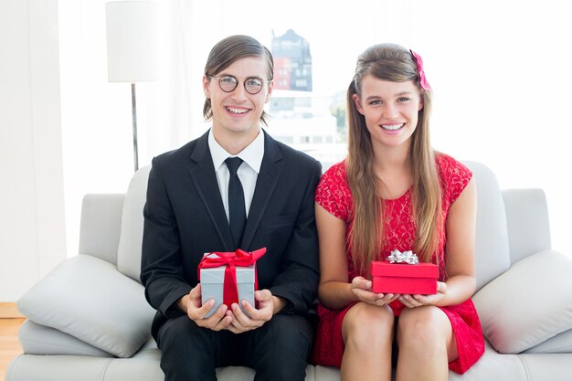 Cute geeky couple smiling and holding gift 