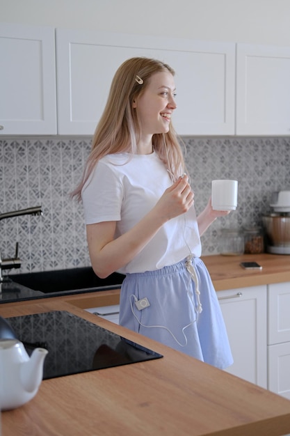 Photo a cute girl of 15-18 years old stands in the kitchen with a mug in her hands