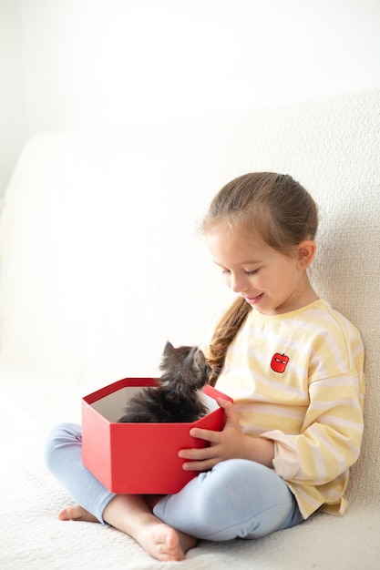 A cute girl of 5 years old receives a kitten in a red box as a gift from her parents Surprise Emotions Congratulation The friendship of a man and a cat