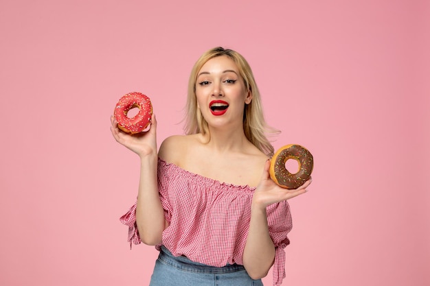 Cute girl adorable blonde chick with red lipstick in pink blouse holding two doughnuts