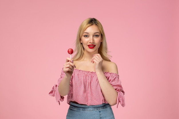 Ragazza carina adorabile giovane donna con rossetto rosso in camicetta rosa che tiene un lecca-lecca rosa rotondo