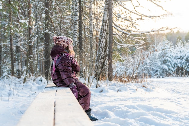 Cute girl on a bench in winter among the snowy forest