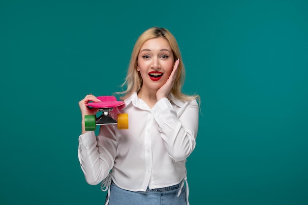 Cute girl blonde beautiful young girl in white neat shirt very happy holding colorful skateboard