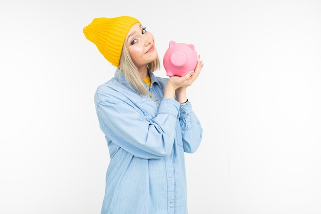 Cute girl in a blue shirt with a bank for saving money on a white background with copy space.