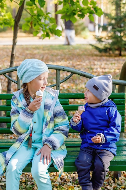 Милая девочка и мальчик, сестра и брат едят мороженое в осеннем парке