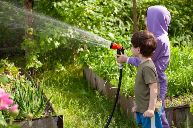 Cute girl and boy watering flowers in the garden at summer day funny kids watering plants in the