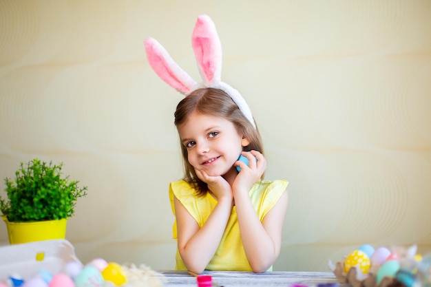 Cute girl in bunnies ears holds easter egg in hand while looking at camera preparing for Easter