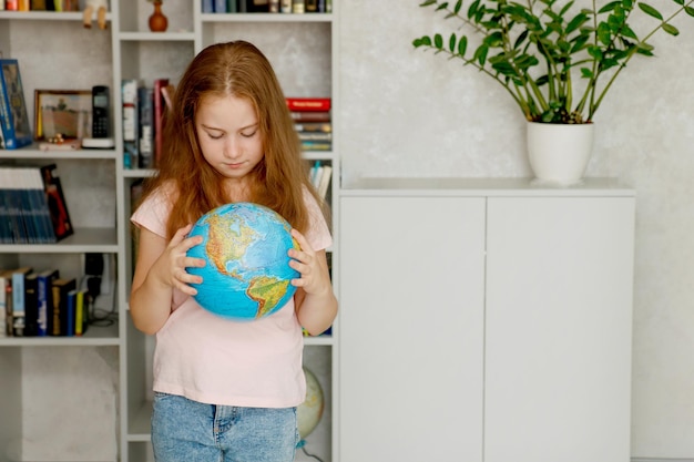 cute girl carefully examines the globe against the background of a bookshelf