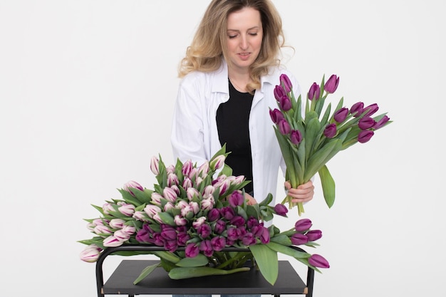 A cute girl chooses a purple tulip for a bouquet on the table Stands on a white background