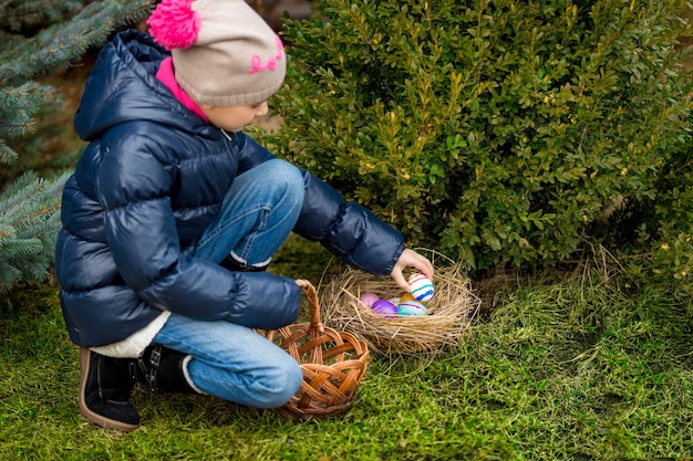 Cute girl collecting colorful Easter eggs in the basket at backyard