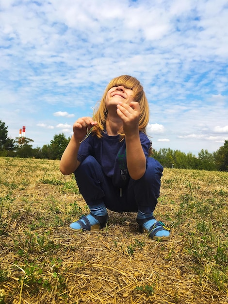 Photo cute girl crouching on field against sky