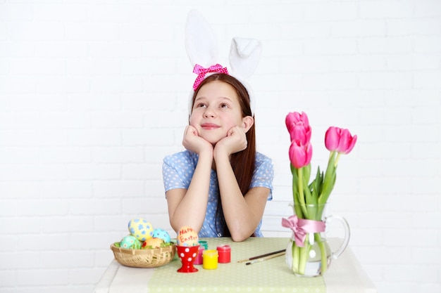 Cute girl decorates Easter eggs, on light background