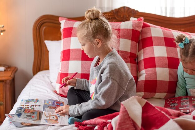 Photo cute girl drawing in book while sitting on bed at home