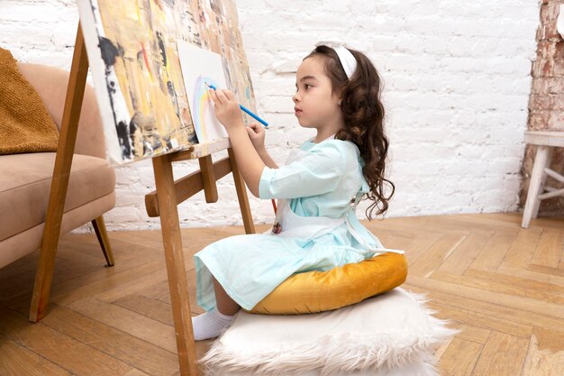 Photo cute girl drawing rainbow on white sheet on a drawing easel little painting artist