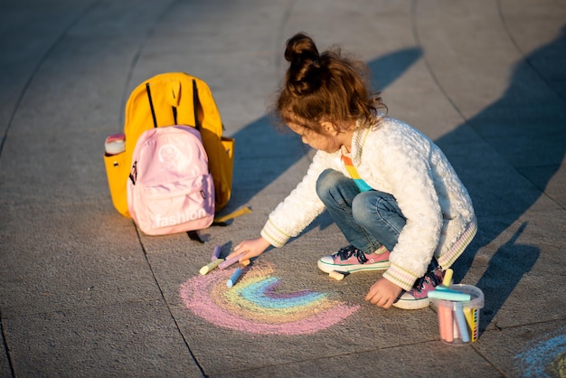 A cute girl draws a rainbow with crayons on the street. Creation. Kids. Street.