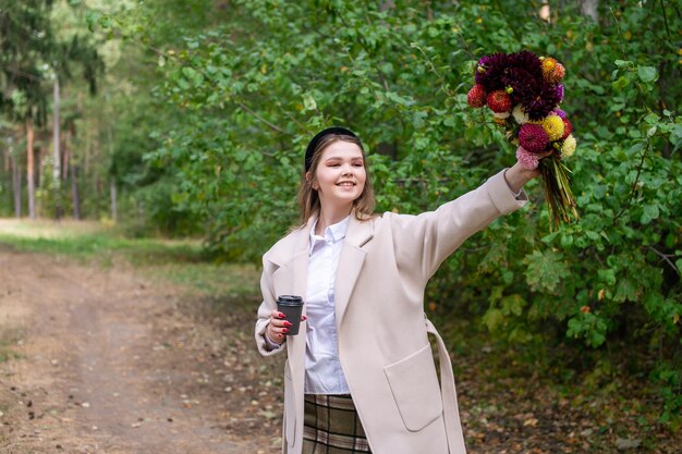 コーヒーを飲むかわいい女の子が花を上げて手を上げた