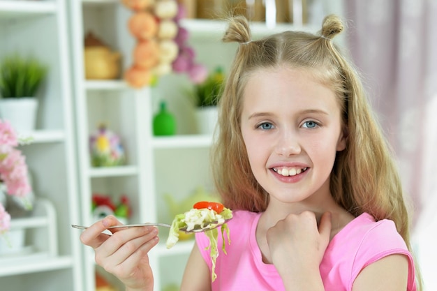 Cute girl eating delicious fresh salad in kitchen at home