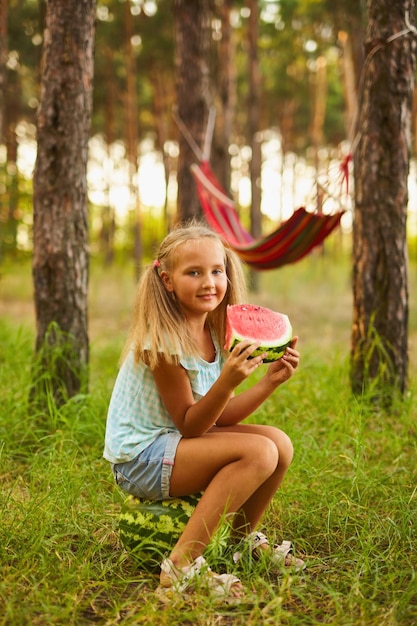 Cute girl eating watermelon at park in the forest