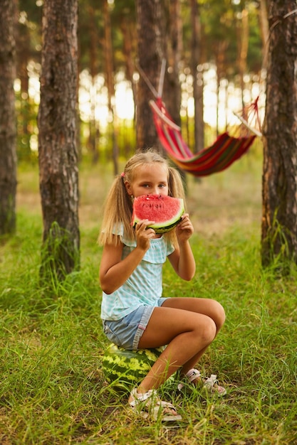 Cute girl eating watermelon at park in the forest