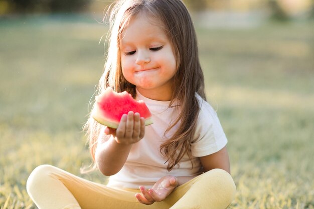 Photo cute girl eating watermelon sitting at park