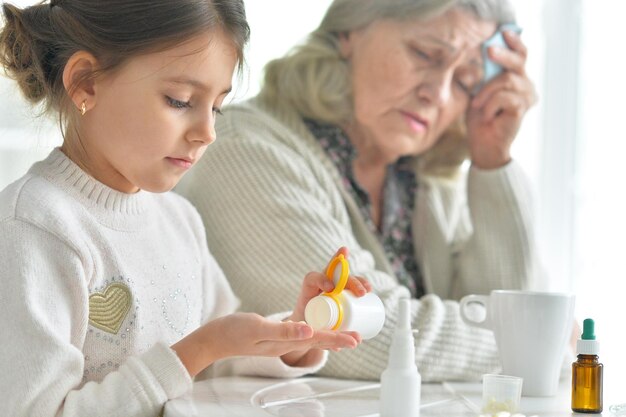 Cute girl giving medicine to sick senior woman