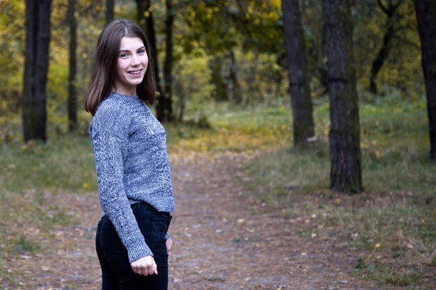 회색 스웨터에 귀여운 소녀는 가을 숲에서 도로에 반 차례입니다.