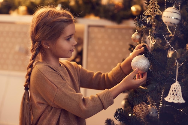 Cute girl hanging Christmas bauble on tree