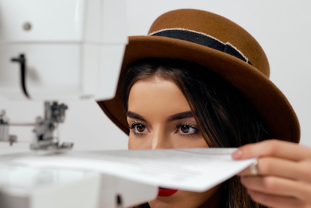 Cute girl in hat uses sewing machine sews paper High quality photo