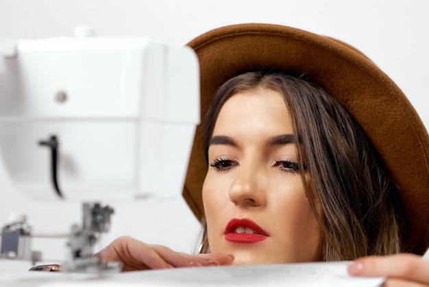 Cute girl in hat uses sewing machine sews paper High quality photo