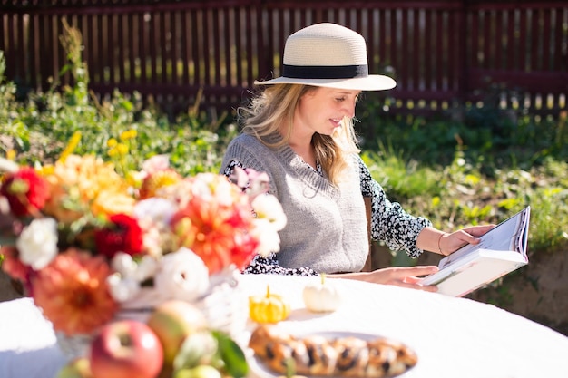 Cute girl in a hat with a brim reading a book at a table outside